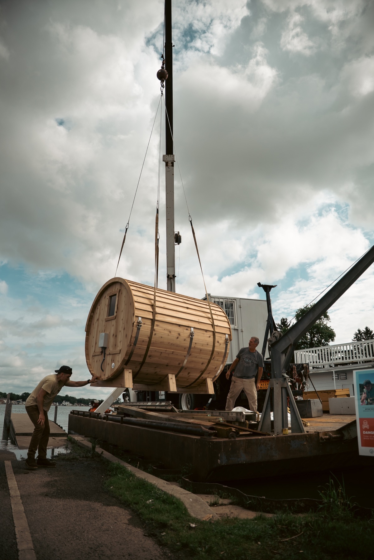 A SISU barrel sauna being lifted onto a barge for delivery